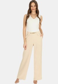 Beżowe spodnie o szerokich nogawkach z paskiem z złotymi akcentami, dwoma przednimi kieszeniami i gładką strukturą, połączone z dopasowaną białą bluzką z dekoltem w serek.