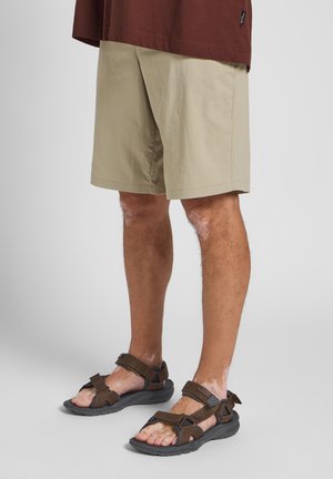 Beige Shorts mit geradem Schnitt, kombiniert mit braunen Sandalen mit Riemen, die verstellbare Riemen und eine robuste Sohle haben.