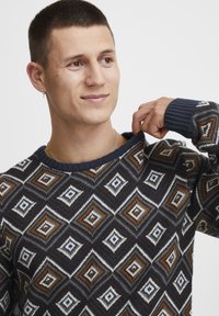 Tmavý pletený sveter s geometrickým vzorom diamantu v bielej, oranžovej a modrej farbe. Hrebienkový výstrih a manžety s uvoľneným strihom.