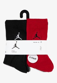 Six paires de chaussettes montantes en noir et rouge, texture côtelée, avec des logos Jumpman blancs et noirs, emballées avec une étiquette indiquant la quantité.