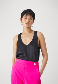 Top in satin nero con design a V profonda, abbinato a pantaloni a vita alta di un vivace rosa con dettagli in bottone dorato.