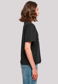 Black cotton t-shirt with short sleeves, relaxed fit, featuring a floral design on the front. Paired with light blue denim jeans.