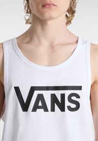 Camiseta sin mangas de algodón blanco con un gran logo negro de "VANS" en el pecho; el diseño incluye un escote redondeado.