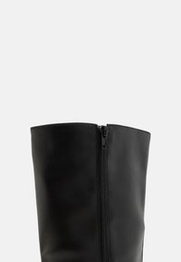 Bottines en cuir noir avec une texture lisse, dotées d'une fermeture éclair sur le côté et d'un bord supérieur droit. Design simple, sans matériel ou motifs supplémentaires.