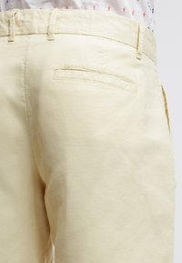 Pantalon jaune pâle en tissu de coton doux, doté d'une poche arrière, de détails cousus et d'une texture lisse. Coupe droite.