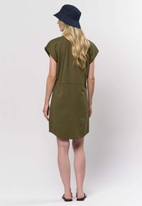 Olivovozelené šaty s krátkymi rukávmi typu cap, okrúhlym výstrihom a zaobleným okrajom. Kombinované s námorníckym modrým klobúkom typu bucket a čiernymi sandálmi.
