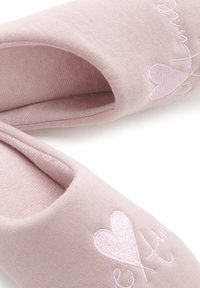 Roze stoffen slippers met een zachte textuur, voorzien van geborduurd hartdetail en sierlijke tekst. Ontwerp met open achterkant voor eenvoudig aan- en uittrekken.