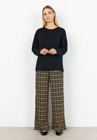 Svart långärmad topp i kombination med vida rutiga byxor i beige och svarta nyanser, med en avslappnad passform och mjukt tyg. Svarta högklackade skor.