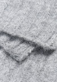 Tissu en tricot gris avec un motif texturé. Le matériau est doux et pelucheux, montrant des fibres torsadées et entrelacées tout au long.