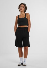 Svart kort topp med fyrkantig halsringning och tjocka axelremmar, matchad med lösa, texturerade svarta shorts med elastisk midja.