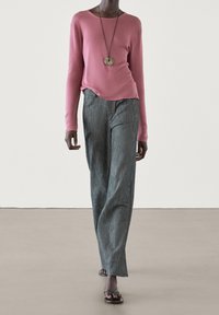 Roze lange mouwen trui, grijs gestreepte wijde broek en zwarte flip-flops. Een hangerketting voegt detail toe aan de outfit.