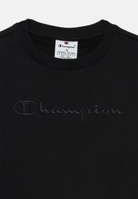 Felpa in cotone nera con logo "Champion" in rilievo sul davanti, collo rotondo e colletto a coste. Dettagli dell'etichetta visibili all'interno.