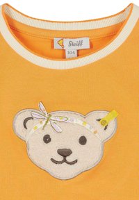 Orange Baumwoll-T-Shirt mit einer Creme-Bärenkopf-Applikation und gestickten Details, einem Haarband und einem Etikett mit Markeninformationen.