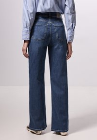 Dark blue wide-leg jeans with a high waist, two back pockets, and a smooth denim texture, paired with a blue and white striped shirt.