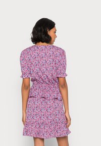 Vestido floral com base rosa e acentos azuis. Apresenta mangas curtas bufantes, cintura franzida e barra com babados. Textura de tecido suave.