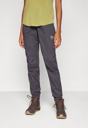 Grau leichte Outdoor-Hosen mit Taschen und einem Logo-Patch, kombiniert mit braunen Wanderschuhen mit Schnürsenkeln und einer Gummisohle.