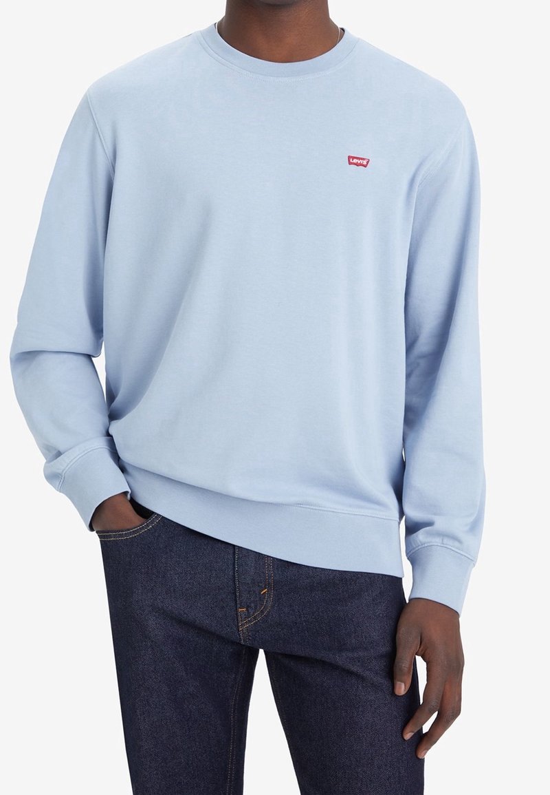 Sudadera de cuello redondo de color azul claro, hecha de suave algodón. Presenta mangas largas y un pequeño logo rojo de Levi's en el pecho. Combinada con jeans de mezclilla oscura.