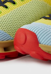 Multicolored athletic shoes featuring a textured mesh upper in yellow and blue, with red rubber accents and a cushioned sole.