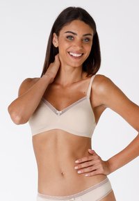 Reggiseno beige in materiale liscio, con bordi in pizzo ondulato, spalline regolabili e chiusura frontale. Design semplice e senza cuciture.