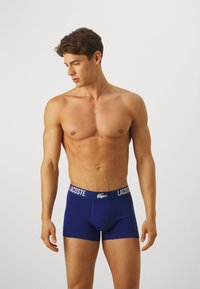 Navy blue boxer briefs with a white Lacoste logo on the waistband. Made of smooth fabric, featuring a fitted shape and stitching details.