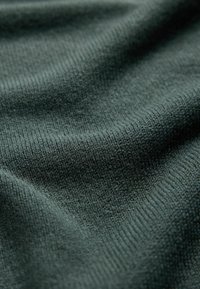 Close-up of soft, dark green knitted fabric with visible texture and gentle folds.