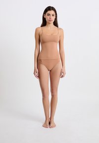 Nagi bezszwowy bodysuit z cienkimi ramiączkami, dopasowany krój i gładka faktura. Dodatkowe pasujące wysokie majtki z minimalnymi detalami szwów.