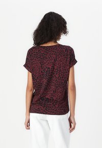 Haut à manches courtes rouge et noir à motif léopard, avec une coupe décontractée et un col rond, fabriqué à partir d'un tissu doux. Motif distinctif sur l'ensemble.