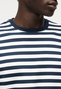 Κοντινό πλάνο ατόμου που φοράει μπλουζάκι με οριζόντιες ριγέ μπλε σκούρο και λευκό χρώμα και στρογγυλή λαιμόκοψη, δείχνοντας τον λαιμό και το κάτω μέρος του προσώπου.