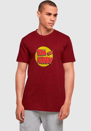 Mørkerød bomulds t-shirt med et cirkulært gult grafik, hvor "TOM og JERRY" står i røde bogstaver. Kortærmet og med rund hals.