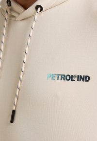 Helle Hoodie aus strukturiertem Stoff mit einem schwarzen und blauen "PETROL IND" Logo und kontrastierenden Kordeln.