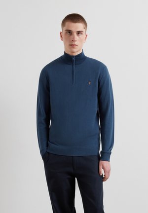 Dunkelblauer Pullover mit hohem Kragen, Reißverschluss und gerippten Bündchen. Mit einem kleinen, unauffälligen Logo in Orange auf der Brust.