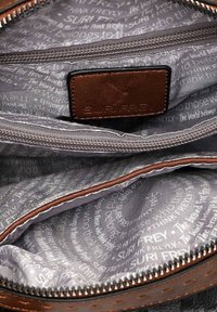 Wnętrze szarej torby z wzorem, z wieloma zamykanymi na zamek kieszeniami oraz brązową skórzaną metką z wytłoczonym napisem "SURI FREY."