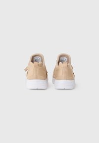 Un paio di sneakers beige con suole bianche viste da dietro, dotate di linguette per il tiro e etichette di taglia visibili all'interno dei talloni.