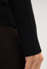Zwarte ribgebreide mouw van een zachte breimateriaal, heeft een aansluitend ontwerp en een gladde textuur met een schone, eenvoudige manchetafwerking.