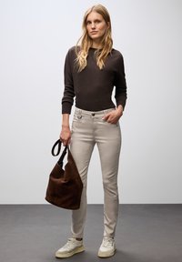 Hnědý pletený svetr, světlé béžové přiléhavé kalhoty, hnědá semišová taška a bílé tenisky s šedými akcenty. Klasický outfit s hladkými liniemi.