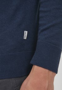 Marineblauer Strickpullover mit gerippten Bündchen und Saum. Verfügt über ein kleines Etikett an der Seite mit "BIBLEND" in weißer Schrift. Glatte Textur.