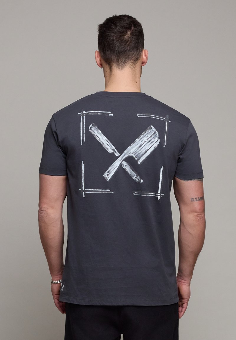 Homme vu de dos portant un t-shirt gris foncé avec un graphique blanc de rasoirs droits croisés encadrés par quatre lignes d'angle dans le dos.