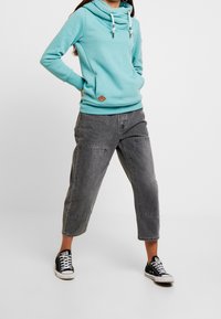 Ljusblå hoodie med kofta och dragsko, kombinerad med grå 3/4-byxor och svarta sneakers. Har en liten logotypdetalj.