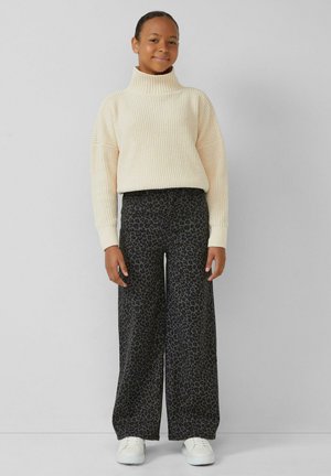 Crème ribbentrui met hoge kraag, gecombineerd met wijde donkere jeans met een subtiel luipaardpatroon. Witte sneakers.