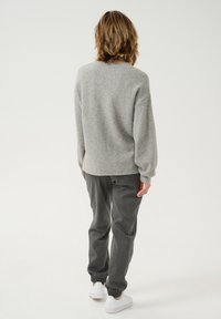 Pulover gri moale cu o croială relaxată, gât rotund și mâneci cu mansete, purtat cu pantaloni relaxați de culoare gri închis și adidași albi.