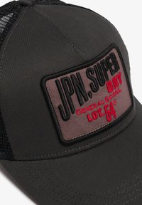 Gorra trucker de malla negra y tela con un parche rectangular que dice "JPN. SUPER DRY GENERAL GOODS LOT.54" en hilo negro y rojo.