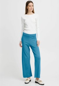 Lichtgewicht, geribbeld wit longsleeve shirt gecombineerd met wijdvallende turquoise broek. De broek heeft een elastische tailleband en een gladde textuur.