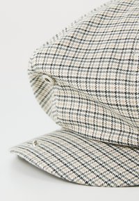 Geruite pet van textuurstof in beige, wit en zwart. Heeft een gebogen klep en metalen accenten aan de zijkanten.