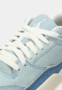 Baskets en denim bleu clair avec des lacets blancs, tige texturée et un accent bleu plus foncé contrasté. Elles présentent un logo sur la languette.