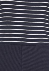 Marinblå och vit randig tyg med en texturerad ribbad mönstring. Har en slät yta upptill och ett diagonalt mönster nertill.