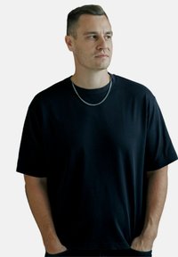 T-shirt nera a maniche corte in misto cotone, caratterizzata da una vestibilità rilassata, collo rotondo e una trama sottile, accessoriata con una collana di catena argentata.