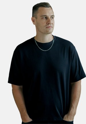 Black short-sleeve t-shirt in cotton blend, featuring a relaxed fit, round neck, and subtle texture, accessorized with a silver chain necklace.