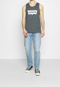 Grå linne med vitt Levi's-logotyp, ljusblå jeans och gröna sneakers. Enkel design, ärmlös skärning och bekväm passform.