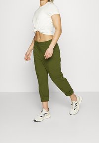 Olivgrön cropped byxor med uppvikta fållar, dragsko i midjan och två framfickor; i kombination med en vit knuten t-shirt och ljusa sneakers.