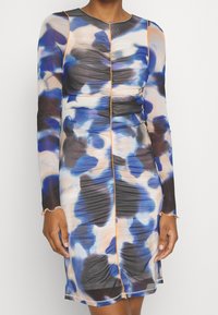Robe à manches longues dans un motif abstrait bleu, noir et crème. Présente des détails froncés et des accents de couture orange.